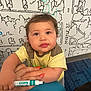 toddler, child, face, marker, hand, yellow_shirt, curly_hair, wall_art, blue_carpet, nails, orange_nail_polish, indoor, cute, expression, person, drawing, playful, young_child, marker_pen, holding