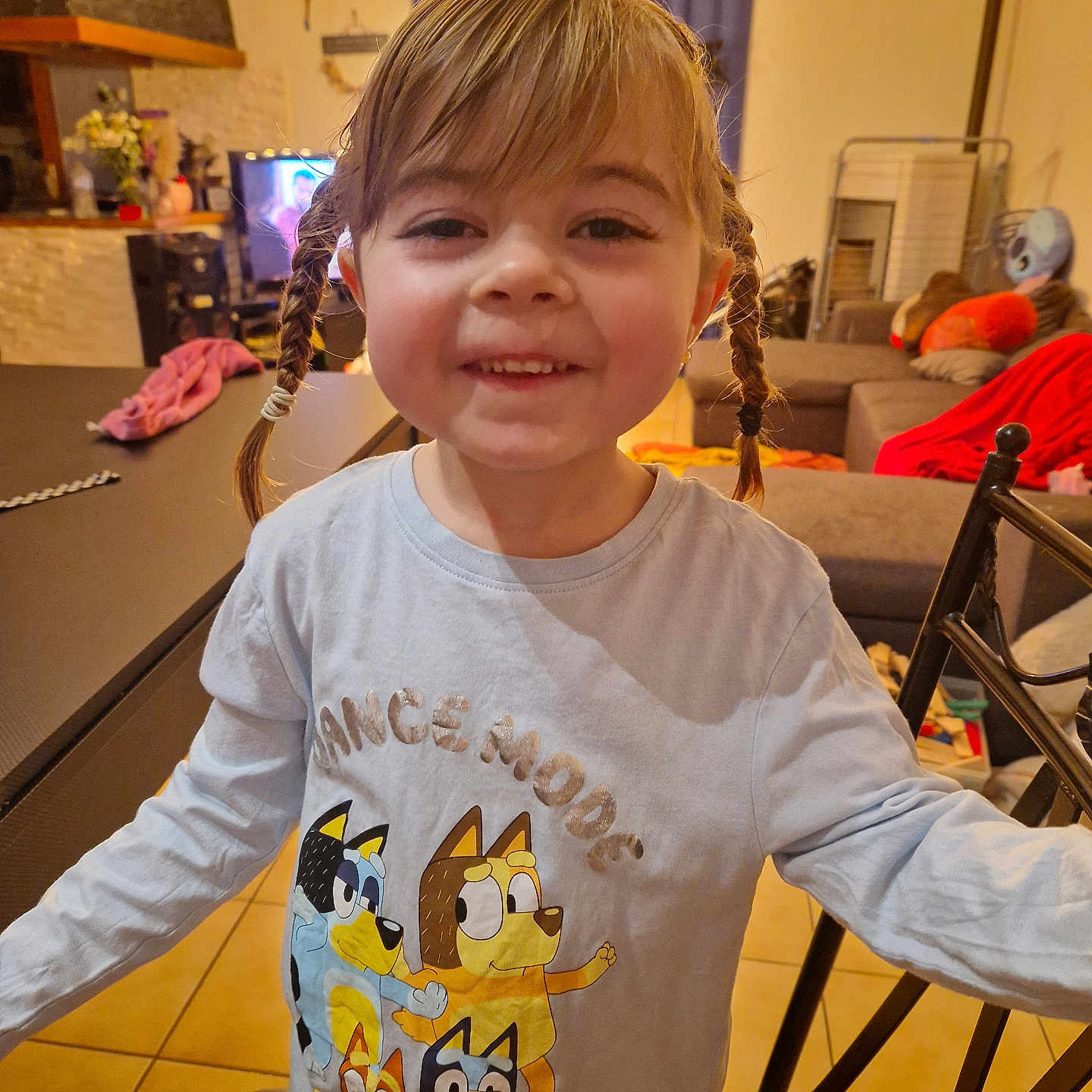 Ombelyne participe au concours pour gagner de l'argent avec cette photo : blanket, braids, cartoon_characters, chair, child, couch, curtains, floor_tiles, furniture, girl, happy, home, indoor, living_room, long_sleeve_shirt, person, smiling, table, television, toy