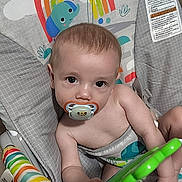 Bruce is registered to the contest to win money with this photo: baby, pacifier, toy, baby_chair, rainbow, sun, monkey, elephant, floor, infant, child, colorful, playtime, cute, indoors, seat, striped, striped_toy, looking_up, young