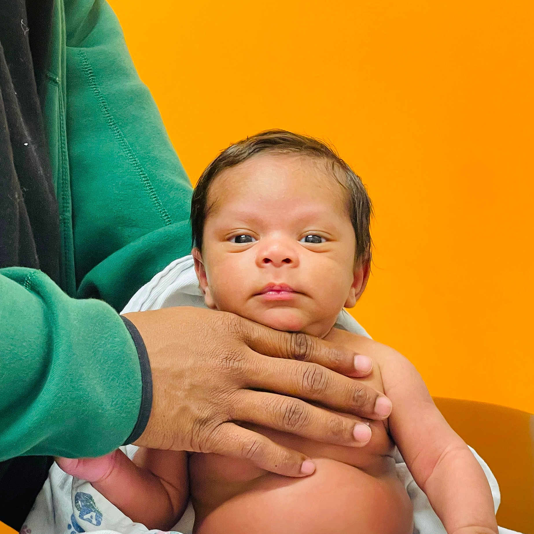 Kingston joined the competition — help win amazing prizes! baby, infant, hand, skin, face, eyes, blanket, orange_background, person, adult_hand, green_sleeve, portrait, newborn, expression, closeup, child, human, young, curious, indoor