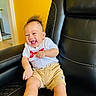baby, child, infant, smiling, laughing, portrait, sitting, chair, leather, furniture, yellow_wall, indoors, home, white_shirt, shorts, sneakers, socks, happy, face, photography
