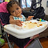 Kennedy joined the competition — help win amazing prizes! toddler, child, baby, high_chair, smiling, eating, snack, food, orange_food, bib, indoor, home, baby_carrier, bookshelf, books, toy, window, curtains, wooden_floor, portrait