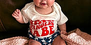 Oaklynn joined the competition — help win amazing prizes! baby, infant, bow, blue_bow, stars, white_shirt, red_text, shorts, star_pattern, blanket, pink_blanket, couch, leather_couch, sitting, cute, child, face, legs, feet, headband