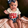 baby, infant, bow, blue_bow, stars, white_shirt, red_text, shorts, star_pattern, blanket, pink_blanket, couch, leather_couch, sitting, cute, child, face, legs, feet, headband