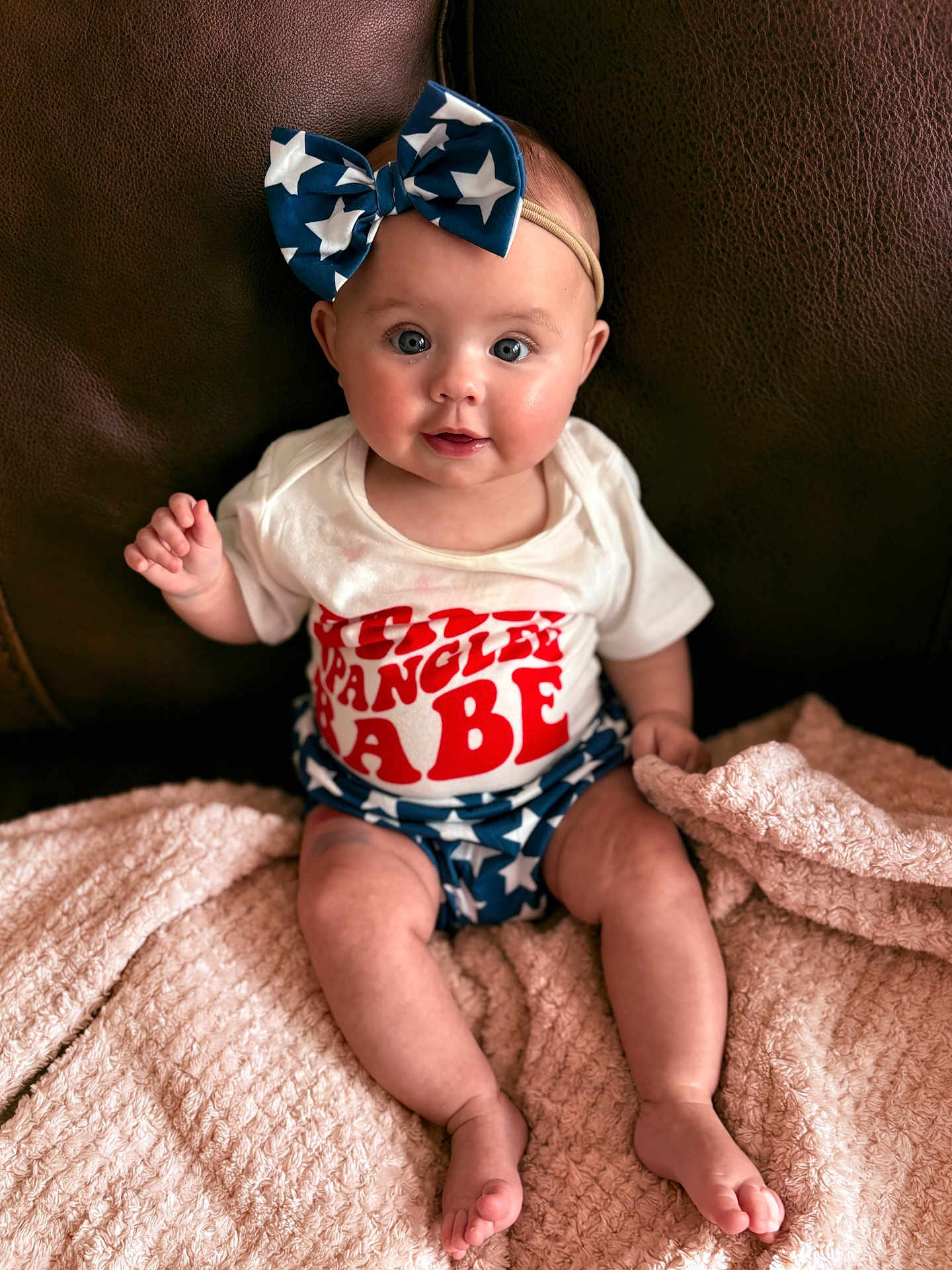Oaklynn joined the competition — help win amazing prizes! baby, infant, bow, blue_bow, stars, white_shirt, red_text, shorts, star_pattern, blanket, pink_blanket, couch, leather_couch, sitting, cute, child, face, legs, feet, headband