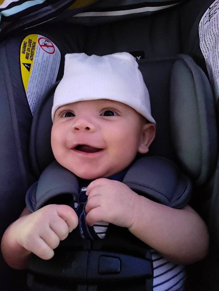 Orion is registered to the contest to win money with this photo: auto_part, baby, baby_carriage, baby_products, baby_toddler_clothing, baseball_cap, cap, car_seat, cheek, child, finger, flash_photography, gesture, happy, hat, headgear, headwear, person, smile, thumb