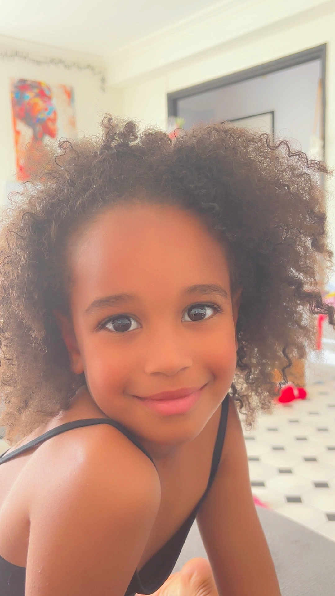 Leyla participe au concours pour gagner de l'argent avec cette photo : child, smile, curly_hair, portrait, indoor, girl, face, happy, person, shoulder, skin, eyes, hair, young, casual, relaxed, warm_light, cozy, artwork, home