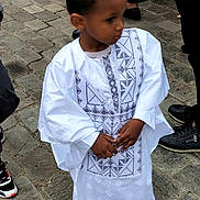 Noah participe au concours pour gagner de l'argent avec cette photo : child, boy, traditional_clothing, white_outfit, embroidery, cobblestone, street, people, shoes, black_shoes, curious, standing, outdoor, hands, portrait, young, fashion, casual, event, culture