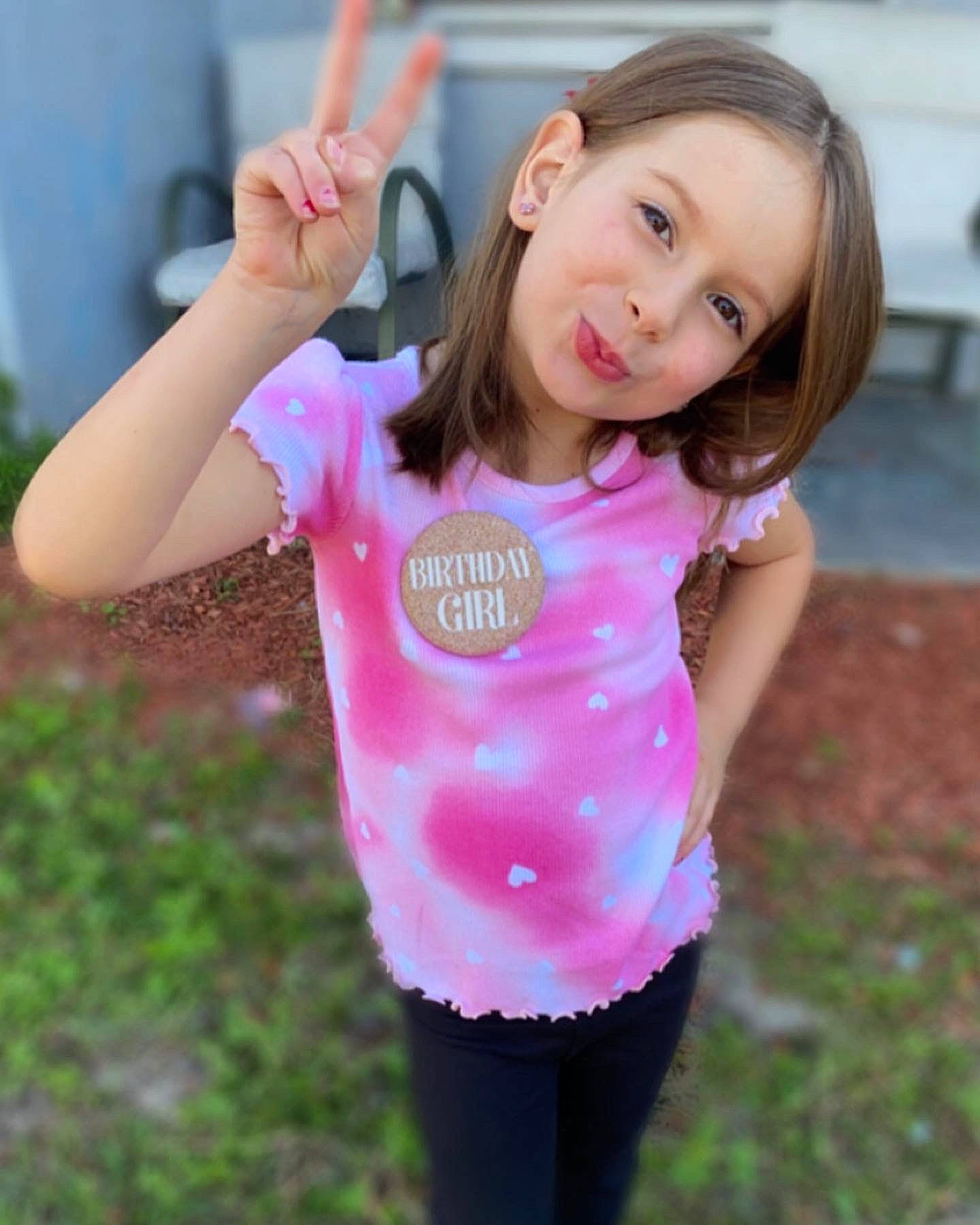Abigale is registered to the contest to win money with this photo: baby_toddler_clothing, beauty, child, face, finger, fun, gesture, grass, hand, happy, head, human_body, magenta, person, pink, sleeve, smile, t_shirt, thumb, toddler