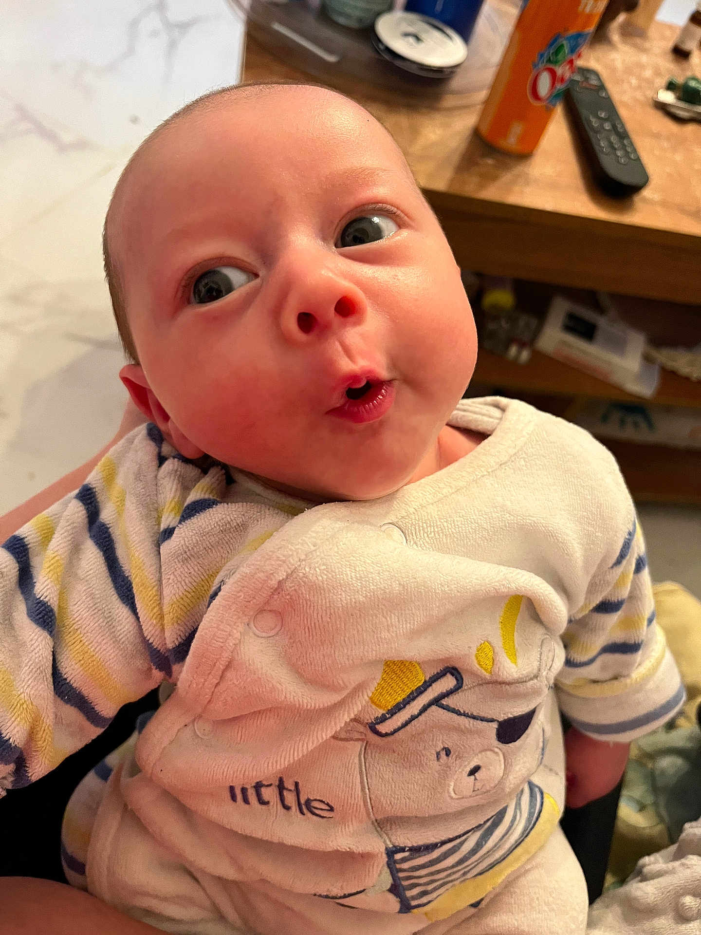 Sasha participe au concours pour gagner de l'argent avec cette photo : baby, infant, child, cute, surprised_expression, striped_clothing, bear_design, indoor, wooden_table, remote_control, can, person_holding, close_up, face, head, eyes, mouth, cozy, soft_fabric, human