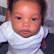 Klarity joined the competition — help win amazing prizes! baby, infant, child, face, eyes, curly_hair, white_clothing, skin, portrait, person, cute, young, hand, indoors, sitting, looking, close_up, human, soft_lighting, expression