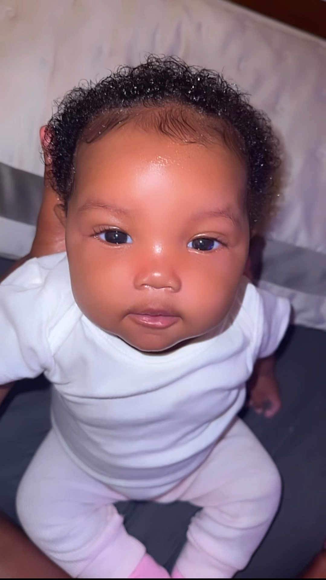Klarity joined the competition — help win amazing prizes! baby, infant, child, face, eyes, curly_hair, white_clothing, skin, portrait, person, cute, young, hand, indoors, sitting, looking, close_up, human, soft_lighting, expression