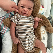 Nova joined the competition — help win amazing prizes! baby, infant, striped_onesie, hand, cheek_pinch, teddy_bear, blanket, bedding, cozy, smile, face, cute, lying_down, soft_texture, person, newborn, child, indoor, expression, cute_face