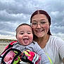 baby, child, woman, glasses, beach, cloudy_sky, blanket, smiling, tongue_out, portrait, outdoor, sand, casual_clothing, person, family, headshot, happy, nature, fun, young_adult