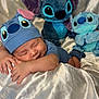 baby, sleeping, hat, blue_outfit, plush_toys, stitch, soft_toys, child, cute, peaceful, fabric, silver, background, indoor, resting, hands, face, headwear, toy, cozy