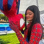 child, person, spiderman, costume, piñata, outdoor, tent, pool, grass, daylight, red, blue, gloves, long_hair, smiling, face, holding, celebration, fun, event