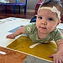 baby, child, headband, blue_eyes, green_shirt, daisy_pattern, carpet, alphabet_rug, hand, floor, indoor, furniture, pink_chair, playroom, curious, portrait, tummy_time, infant, cute, home