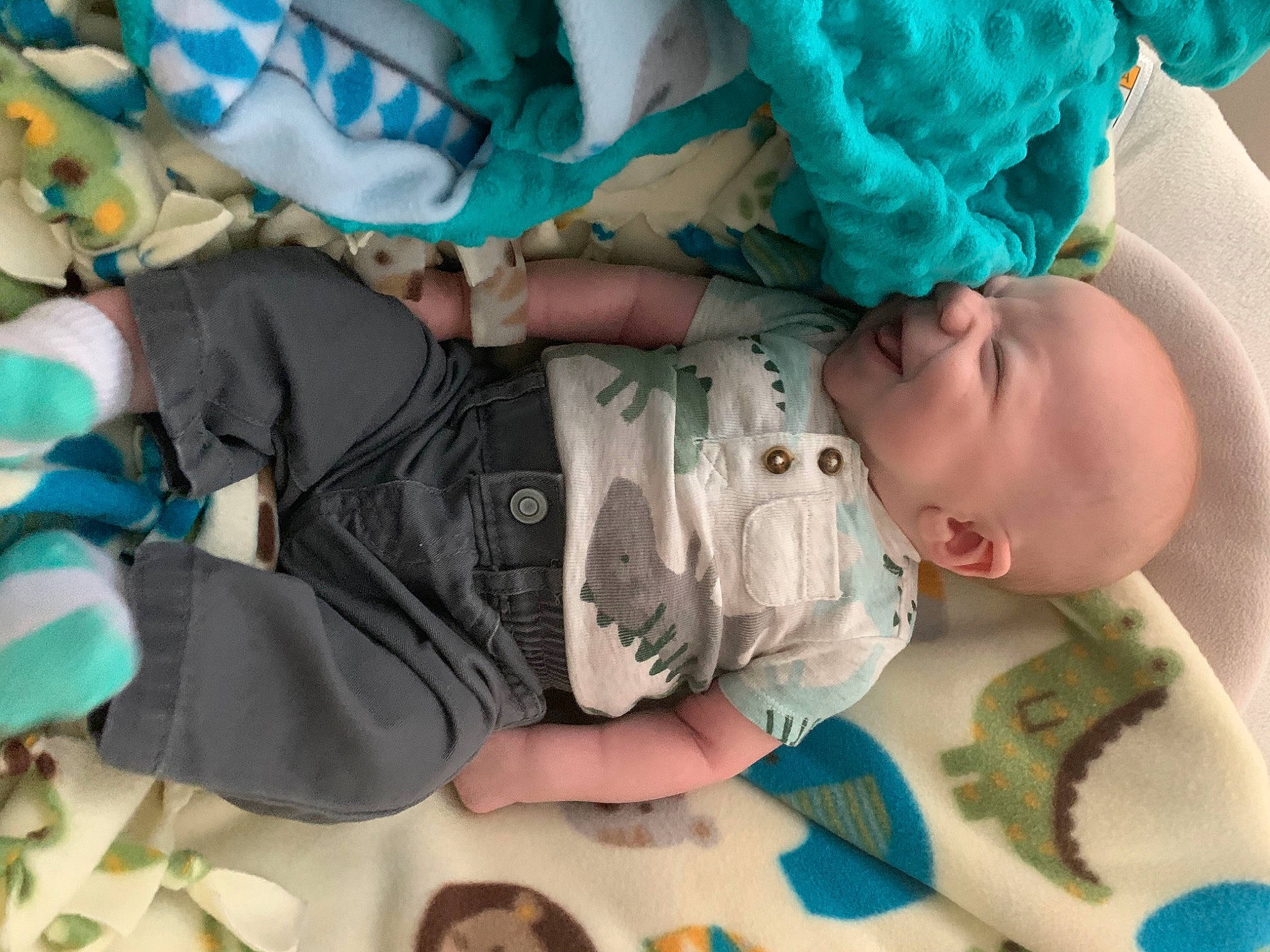 Colton is registered to the contest to win money with this photo: baby, baby_products, baby_sleeping, baby_toddler_clothing, blue, cheek, child, comfort, electric_blue, finger, green, human_body, linens, nail, pattern, person, personal_protective_equipment, room, sitting, textile