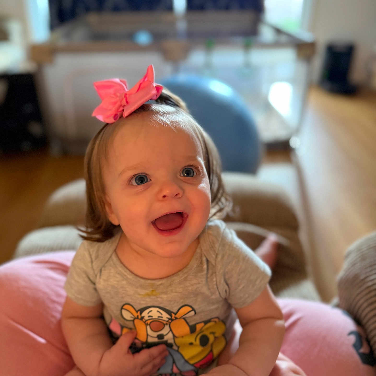 Larae is registered to the contest to win money with this photo: baby, child, smiling, bow, pink_bow, tshirt, tigger, winnie_the_pooh, blue_eyes, happy, indoor, blurred_background, person, cute, sitting, infant, playful, light, face, portrait