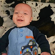 Nathan joined the competition — help win amazing prizes! baby, infant, smiling, onesie, embroidered_car, blue_clothing, blanket, patterned_blanket, face, bald_head, hand, lying_down, cozy, indoor, soft_texture, happy, close_up, baby_clothes, infant_portrait, cute