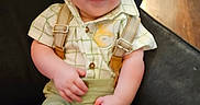 Nathan is registered to the contest to win money with this photo: baby, child, smile, suspenders, green_shorts, checkered_shirt, chair, indoor, wooden_floor, person, happy, cute, infant, seated, portrait, clothing, face, skin, baby_fashion, one_person