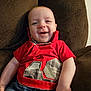 Nathan is registered to the contest to win money with this photo: baby, infant, smiling, red_shirt, plaid_applique, recliner, brown_fabric, sitting, portrait, happy, cute, chubby_cheeks, hand, indoor, home, cozy, closeup, casual_clothing, person, toddler