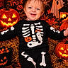 baby, child, smiling, halloween, skeleton_costume, pumpkin, jack_o_lantern, ghost, hay, portrait, indoor, festive, orange_lighting, costume, infant, sitting, face, skeleton, spooky, celebration