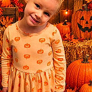 Paisley is registered to the contest to win money with this photo: child, toddler, girl, smiling, portrait, autumn, halloween, pumpkins, jack_o_lantern, orange_dress, leaves, hay_bale, warm_lighting, indoors, fall_decorations, festive, head_tilt, blonde_hair, standing, photography