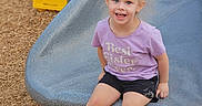 Paisley joined the competition — help win amazing prizes! child, smiling, playground, slide, purple_shirt, shorts, sneakers, outdoor, wood_chips, yellow_play_equipment, happy, blond_hair, pony_tail, casual_clothing, sitting, daylight, fun, person, cute, youth