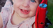 Isabella is registered to the contest to win money with this photo: baby, blue_eyes, child, cute, face, floral_pattern, green_background, happy, infant, outdoor, person, pink_clothing, portrait, red, sitting, skin, smile, stroller, teeth, young_child