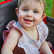 Isabella is registered to the contest to win money with this photo: toddler, child, smiling, blue_eyes, outdoor, green_grass, red_chair, gray_chair, pink_clothing, ruffled_sleeves, sitting, happy, cute, portrait, baby, person, face, skin, sunlight, nature