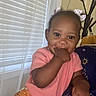 Honey is registered to the contest to win money with this photo: child, baby, toddler, smiling, portrait, sitting, indoor, pink_shirt, floral_pants, hair_bows, finger_in_mouth, window, blinds, chair, star_pattern, coat_rack, home, natural_light, colorful_clothing, happy