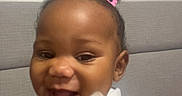 Honey joined the competition — help win amazing prizes! baby, child, infant, smiling, happy, laughing, portrait, face, person, indoor, home, sofa, seated, hair_bow, curly_hair, floral_clothing, white_outfit, close_up, casual_photo, joyful
