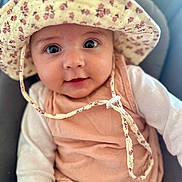 Capucine a rejoint le concours — aidez-le/la à gagner de superbes lots ! baby, infant, hat, floral_hat, cute, portrait, face, eyes, smile, clothing, peach_outfit, white_sleeves, child, young_child, indoors, soft_light, close_up, headwear, baby_girl, seated