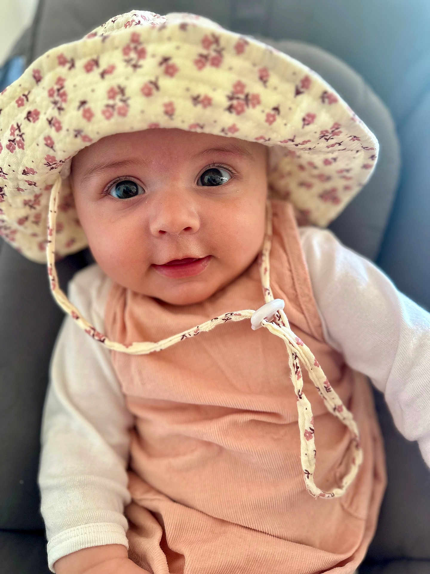 Capucine a rejoint le concours — aidez-le/la à gagner de superbes lots ! baby, infant, hat, floral_hat, cute, portrait, face, eyes, smile, clothing, peach_outfit, white_sleeves, child, young_child, indoors, soft_light, close_up, headwear, baby_girl, seated
