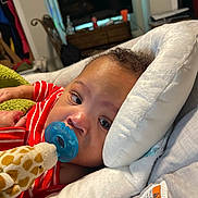 Kaison is registered to the contest to win money with this photo: baby, pacifier, toy, giraffe, pajamas, red_stripes, cushion, white, face, infant, child, indoor, bedroom, blanket, furniture, soft_toy, home, comfort, portrait, closeup