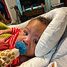 baby, pacifier, toy, giraffe, pajamas, red_stripes, cushion, white, face, infant, child, indoor, bedroom, blanket, furniture, soft_toy, home, comfort, portrait, closeup