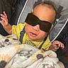 baby, child, sunglasses, blanket, yellow_shirt, baby_seat, infant, hand, face, curly_hair, cozy, comfort, indoor, cute, fashion, portrait, expression, casual, relaxing, young