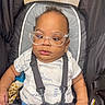 baby, child, glasses, car_seat, straps, calvin_klein, shirt, blue_pants, toy, giraffe_toy, curly_hair, pout, cute, indoor, infant, person, seat, sitting, closeup, expression
