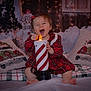 toddler, child, candle, plaid_dress, holiday_decor, christmas_pillows, snowman, festive_lights, winter_scene, indoor, cute, smiling, happy, decorative_candle, holiday_season, cozy, red_bow, cheerful, sitting, portrait