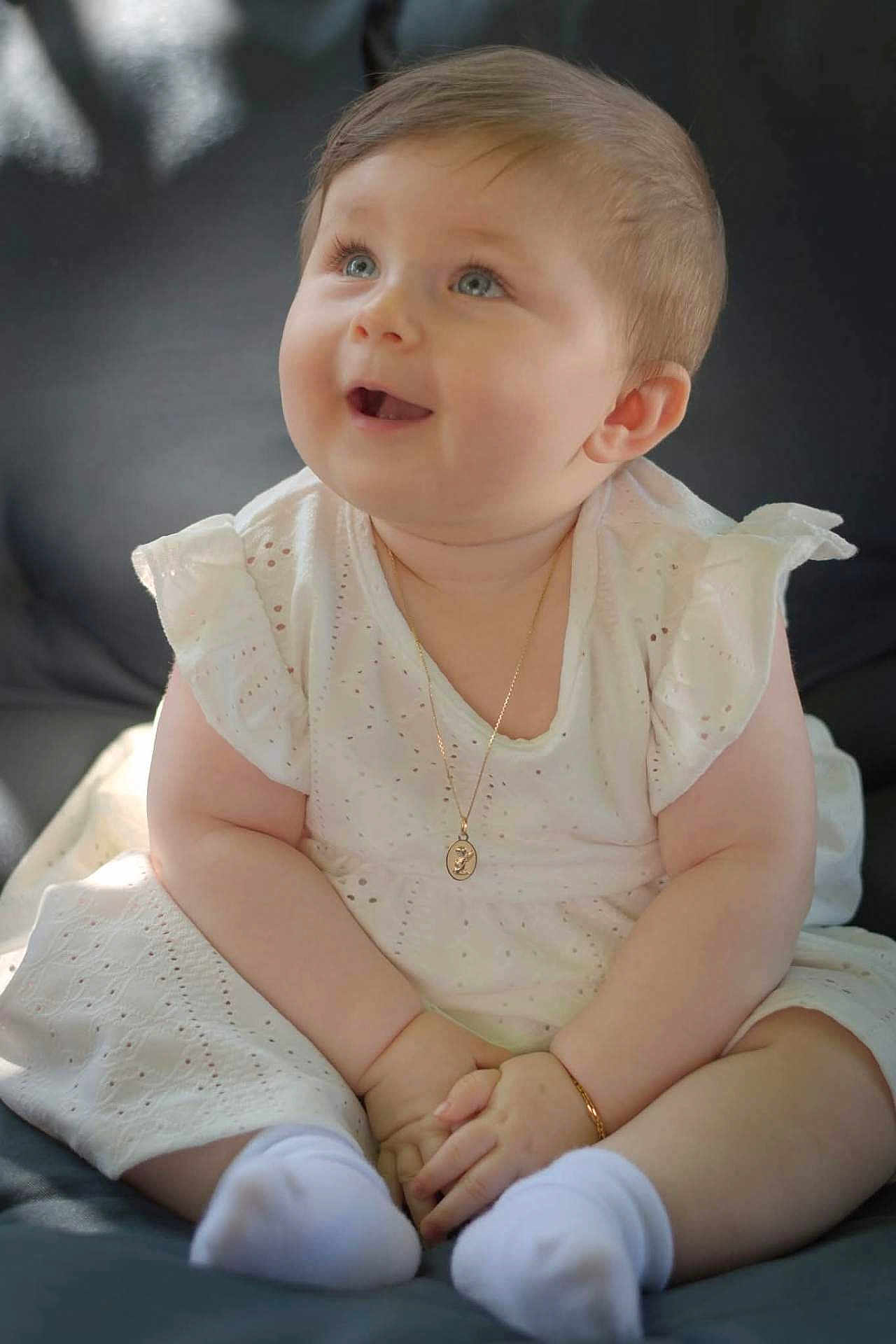 Esmée a rejoint le concours — aidez-le/la à gagner de superbes lots ! baby, child, white_dress, sitting, smile, happy, blue_eyes, bracelet, necklace, sock, cute, chubby, portrait, indoors, soft_light, couch, skin, short_hair, infant, hands