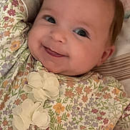 Oaklynn is registered to the contest to win money with this photo: baby, smiling, infant, face, floral_outfit, flower_pattern, lying_down, crib, pink, white, cute, child, young, happy, portrait, soft_lighting, indoors, cozy, comfort, person