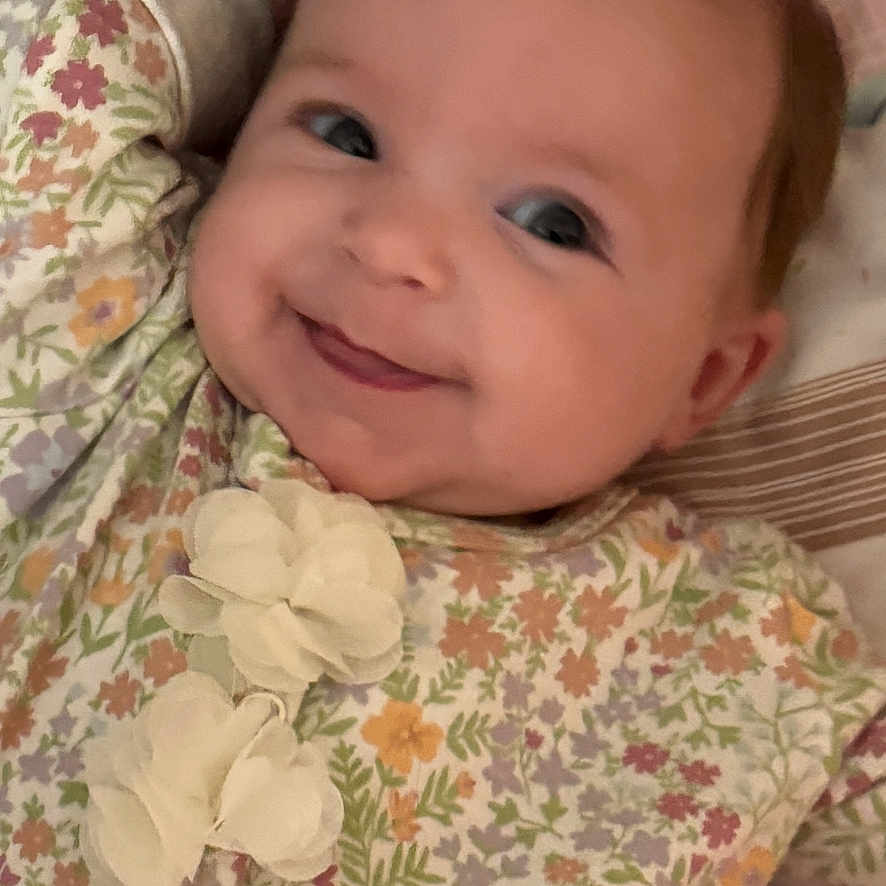 Oaklynn is registered to the contest to win money with this photo: baby, smiling, infant, face, floral_outfit, flower_pattern, lying_down, crib, pink, white, cute, child, young, happy, portrait, soft_lighting, indoors, cozy, comfort, person