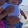 baby, child, smiling, hat, striped_clothing, blue, beach, sea, sunny, sky, person, holding, summer, outdoor, water, shore, cute, infant, portrait, sunlight
