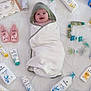 baby, smiling, towel, hood, white_sheet, baby_care_products, bottles, tubes, pacifiers, skincare, cream, lotion, baby_bath, infant, happy, wrapped, cute, product_arrangement, biolane, soft