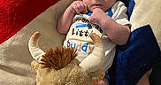 Dean is registered to the contest to win money with this photo: adult_arm, baby, blanket, child, clothing, couch, cozy, hands, horns, indoor, infant, lying_down, moose, newborn, onesie, plush_toy, portrait, stuffed_animal, tattoo, wide_eyed