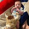 adult_arm, baby, blanket, child, clothing, couch, cozy, hands, horns, indoor, infant, lying_down, moose, newborn, onesie, plush_toy, portrait, stuffed_animal, tattoo, wide_eyed