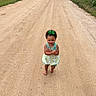 Kaizlee is registered to the contest to win money with this photo: toddler, child, barefoot, dress, green_bow, dirt_road, rural, outdoor, field, grass, crossed_arms, walking, nature, summer, small_person, sunny, isolated, expression, portrait, scenery