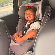 Kaizlee is registered to the contest to win money with this photo: baby, car_interior, car_seat, child, child_safety, clothing, cute, earrings, happy, infant, portrait, red_bow, safety_harness, seat, seatbelt, smiling, sunlight, toddler, travel, window