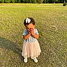 blue_top, bow, child, covering_face, cute, daylight, field, forest, girl, grass, nature, outdoor, pink_skirt, shy, standing, sunlight, toddler, trees, white_shoes, young_child